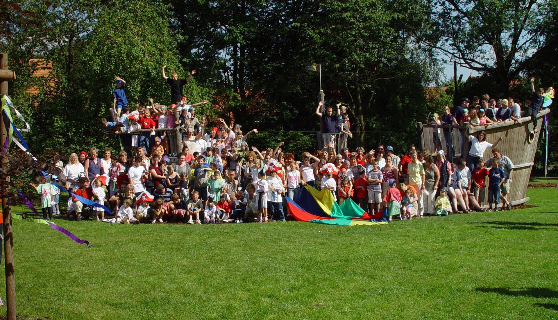 Eine große Gruppe von Erwachsenen und Kindern steht an einem Spielgerät, das wie ein Piratenschiff aussieht.